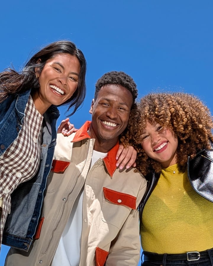 Three people smile side-by-side with the sky as backdrop